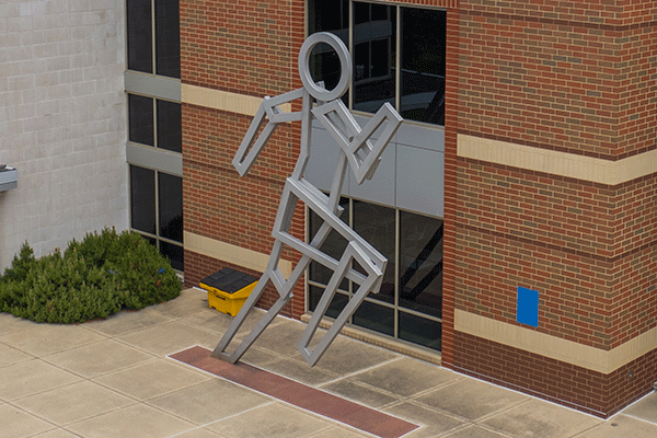 Aerial photo of a large building with a metal statue shaped as a runner in front of the structure.